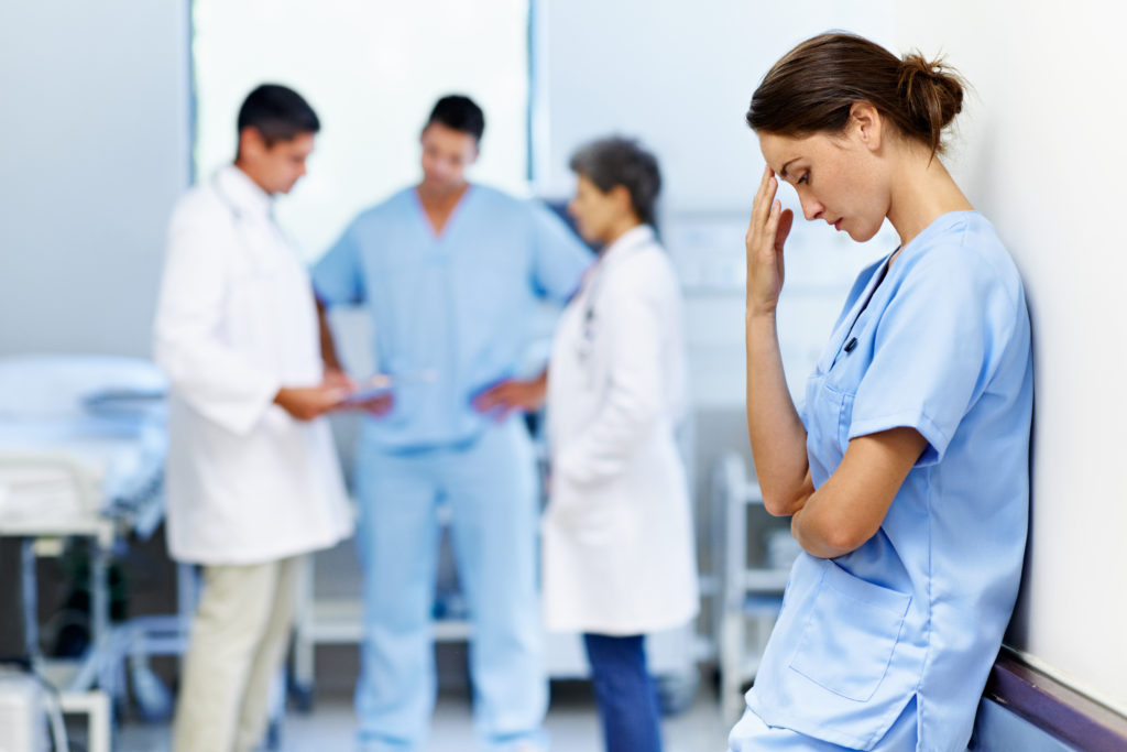 Shot of an exhausted doctor leaning against a wall with colleagues in the background
